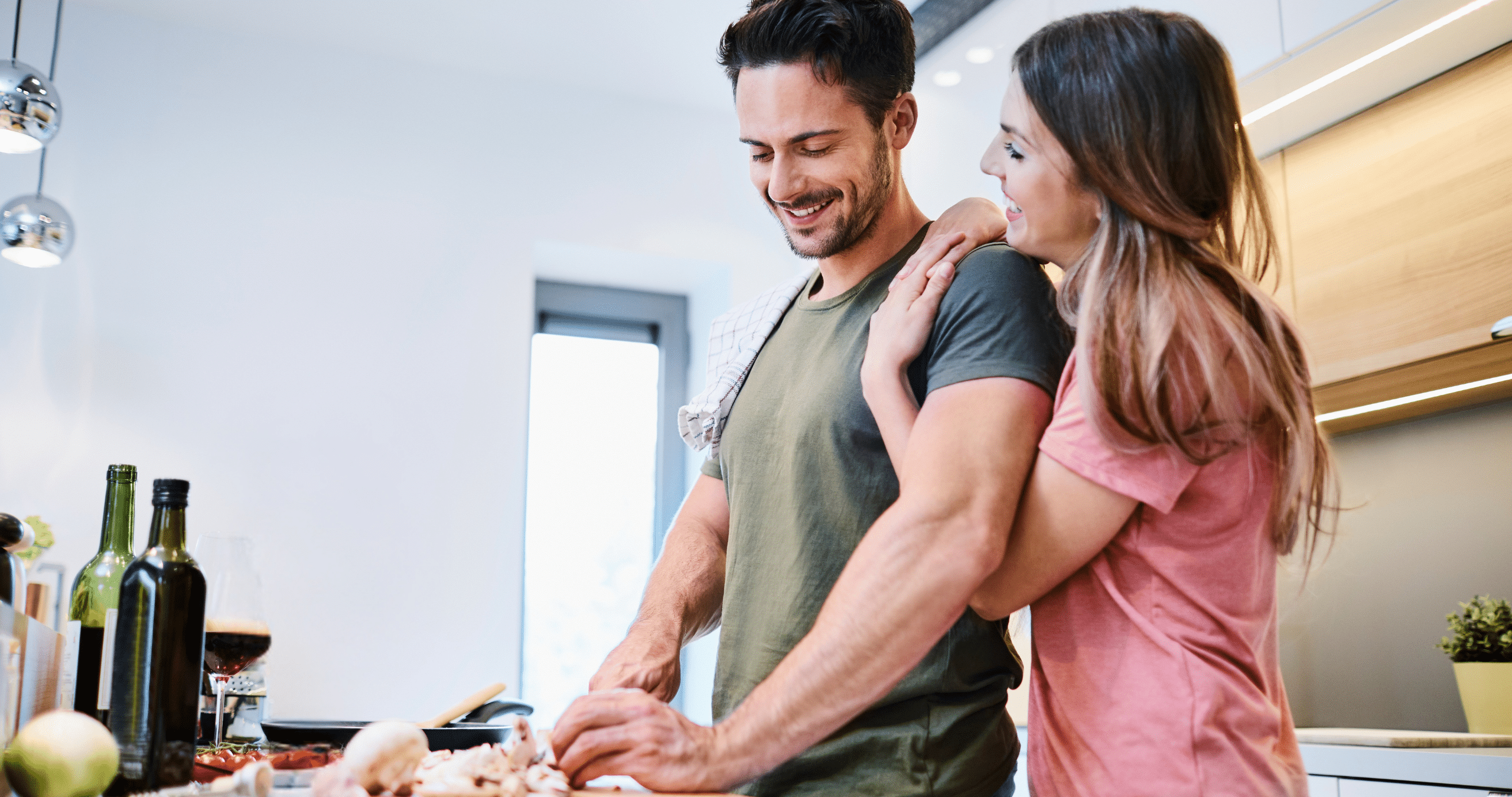 Woman with arms around man while in kitchen, smiling