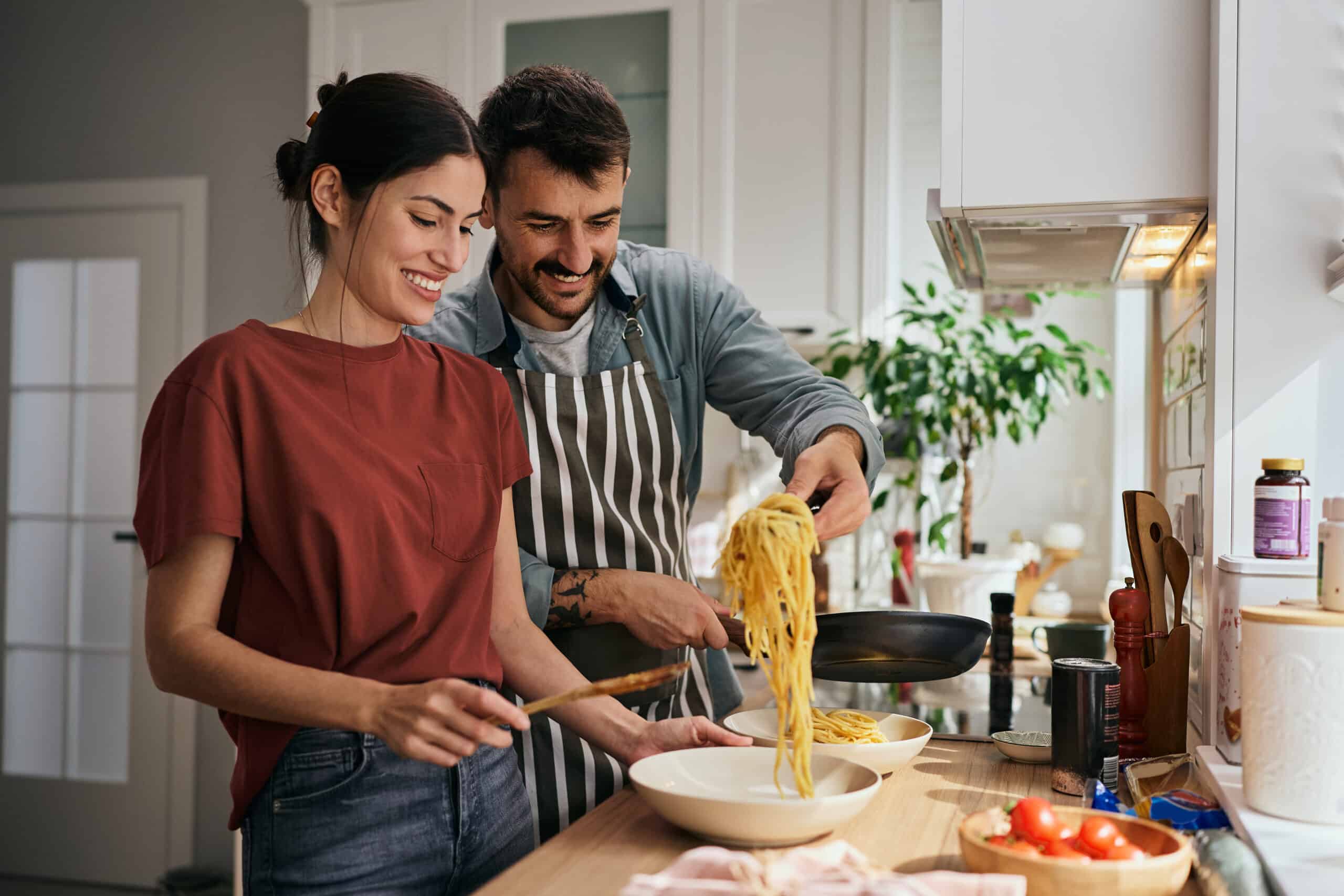Couple in kitchen, smiling and cooking together
